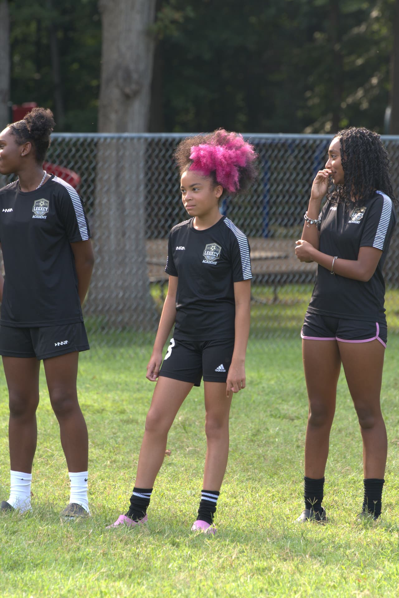 Three Legacy Lionesses standing together on the sideline in academy kit